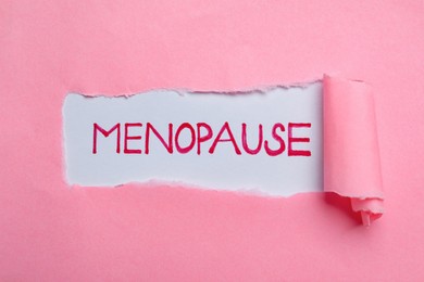 Photo of Word Menopause written on white background, view through hole in pink paper