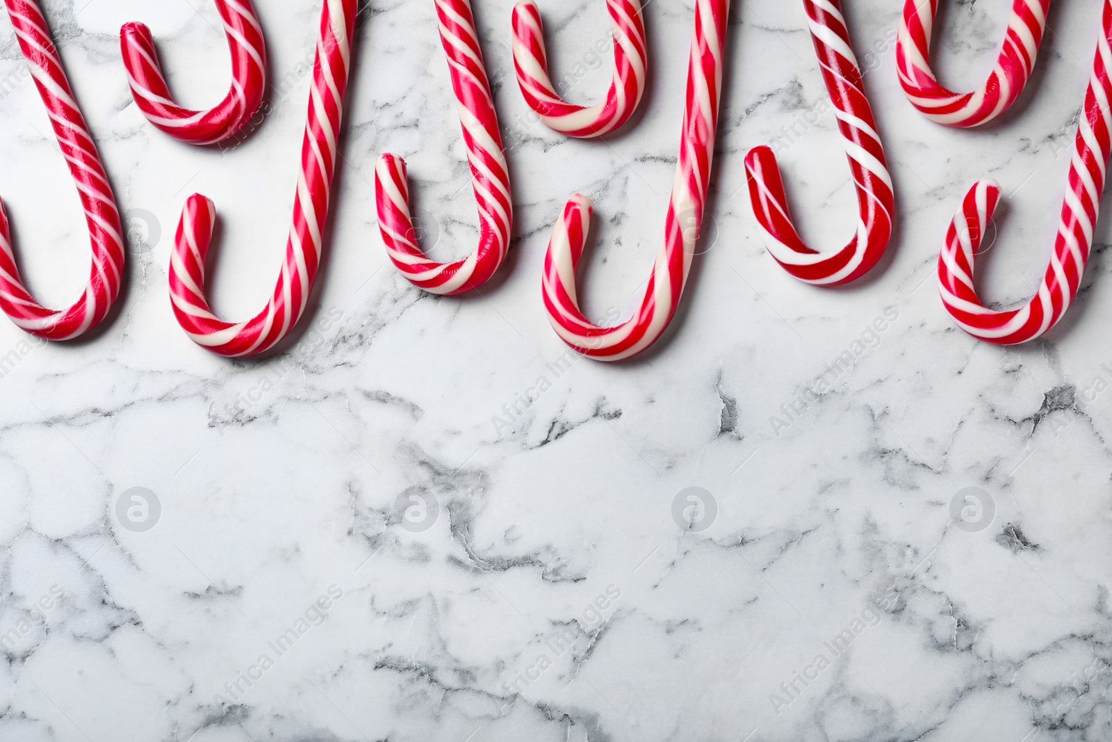 Photo of Sweet Christmas candy canes on white marble background, flat lay. Space for text