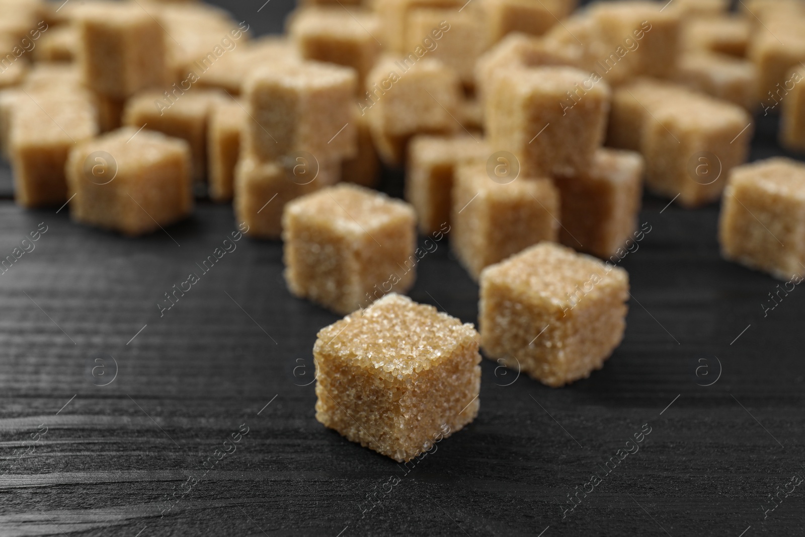 Photo of Brown sugar cubes on black wooden table, closeup