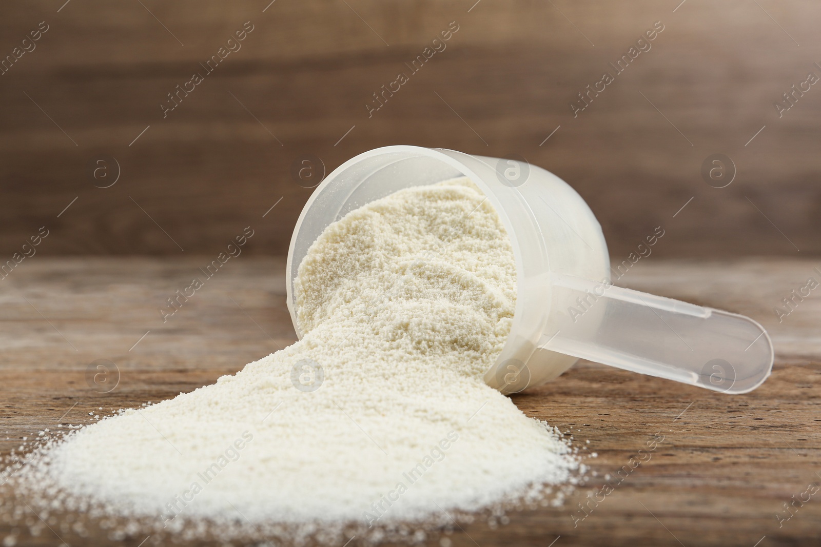 Photo of Overturned measuring scoop with protein powder on wooden table, closeup