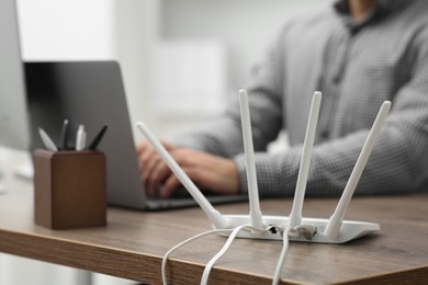 Photo of Man with laptop working at wooden table indoors, focus of Wi-Fi router