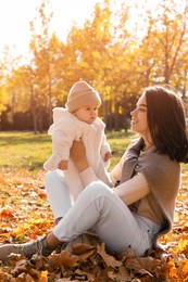 Photo of Happy mother with her baby son sitting on fallen leaves in autumn park