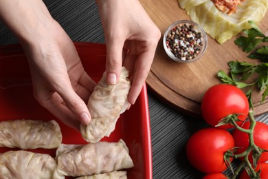 Woman putting uncooked stuffed cabbage roll into baking dish at black table, top view