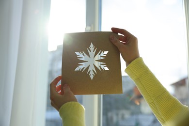 Photo of Woman holding snowflake stencil near window at home, closeup