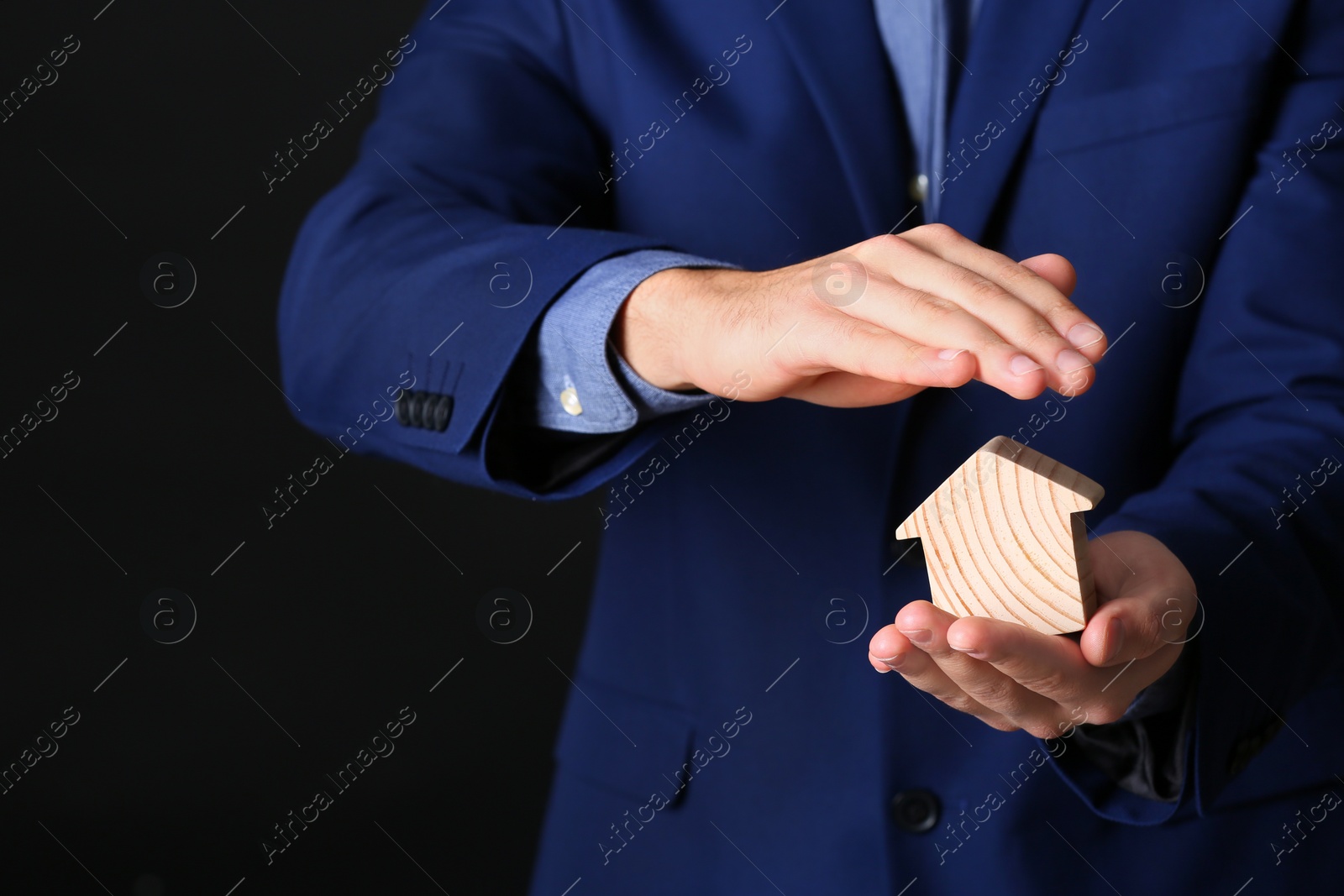 Photo of Male agent covering wooden house on black background, closeup. Home insurance