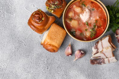 Photo of Delicious borsch served with pampushky and salo on grey textured table, flat lay and space for text. Traditional Ukrainian cuisine