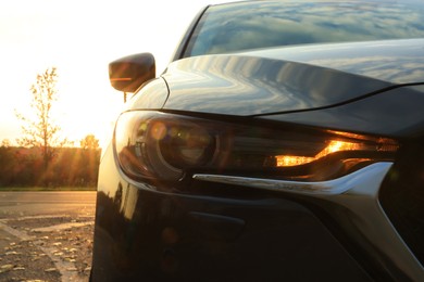Photo of Black modern car parked on road at sunset, closeup of headlight