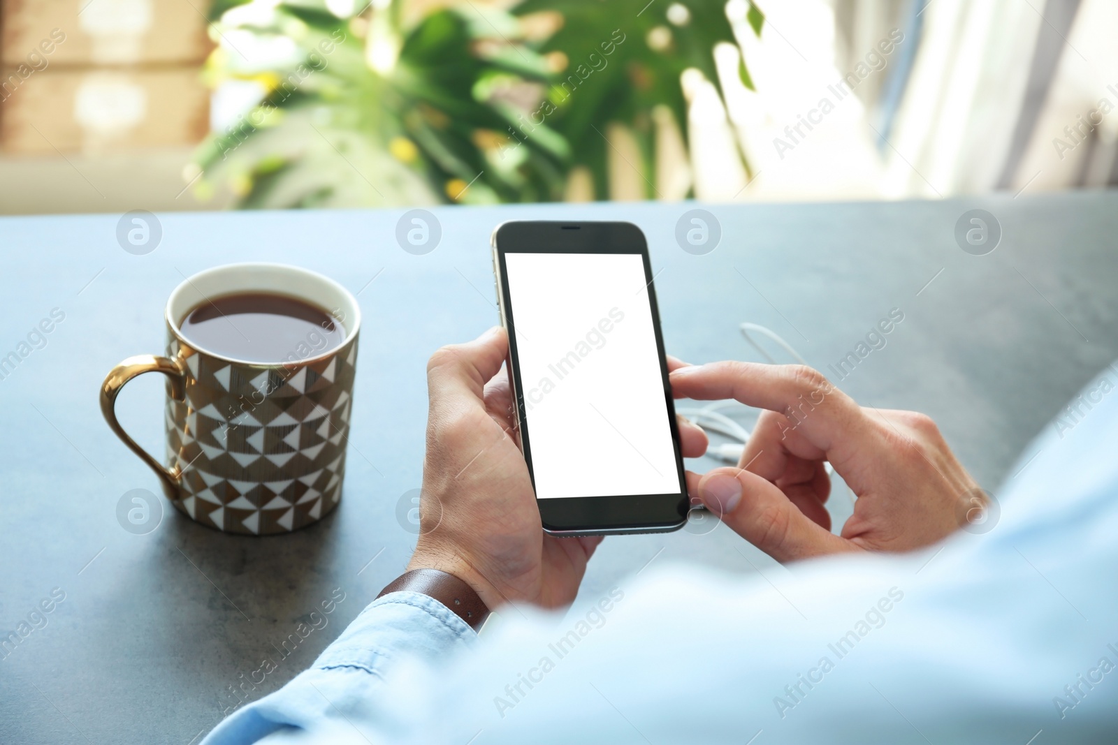 Photo of Young man holding mobile phone with blank screen in hand over table