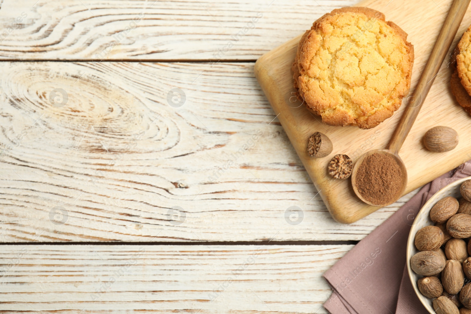 Photo of Nutmeg powder, seeds and tasty cookies on white wooden table, flat lay. Space for text