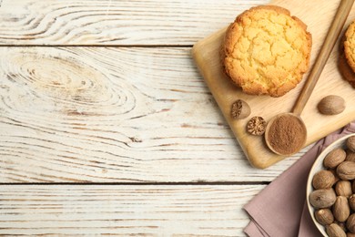 Photo of Nutmeg powder, seeds and tasty cookies on white wooden table, flat lay. Space for text