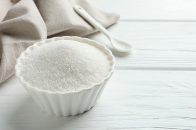 Photo of Granulated sugar in bowl on white wooden table, closeup. Space for text