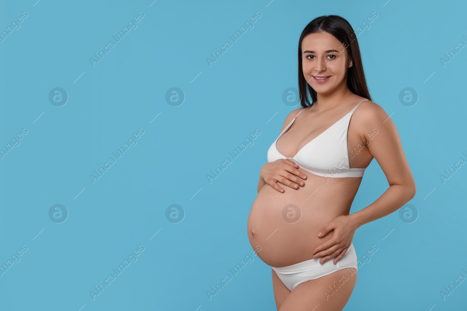 Photo of Beautiful pregnant woman in stylish comfortable underwear on light blue background, space for text