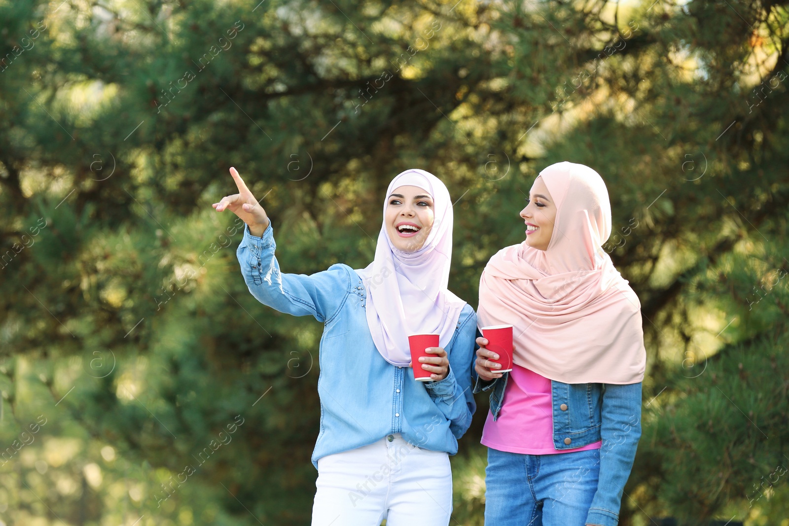 Photo of Muslim women with cups of coffee walking in park