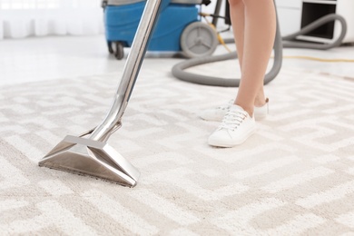 Female worker removing dirt from carpet with professional vacuum cleaner indoors