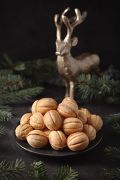 Plate of tasty nut shaped cookies among fir branches on black table