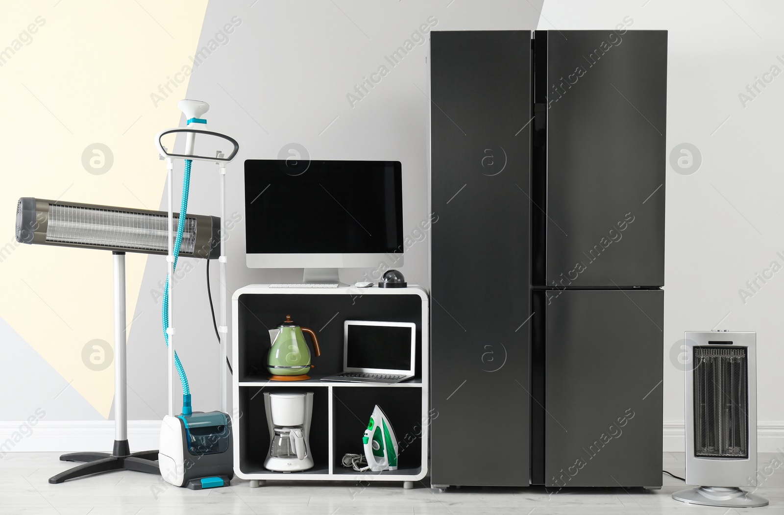 Photo of Modern refrigerator and other household appliances near color wall indoors