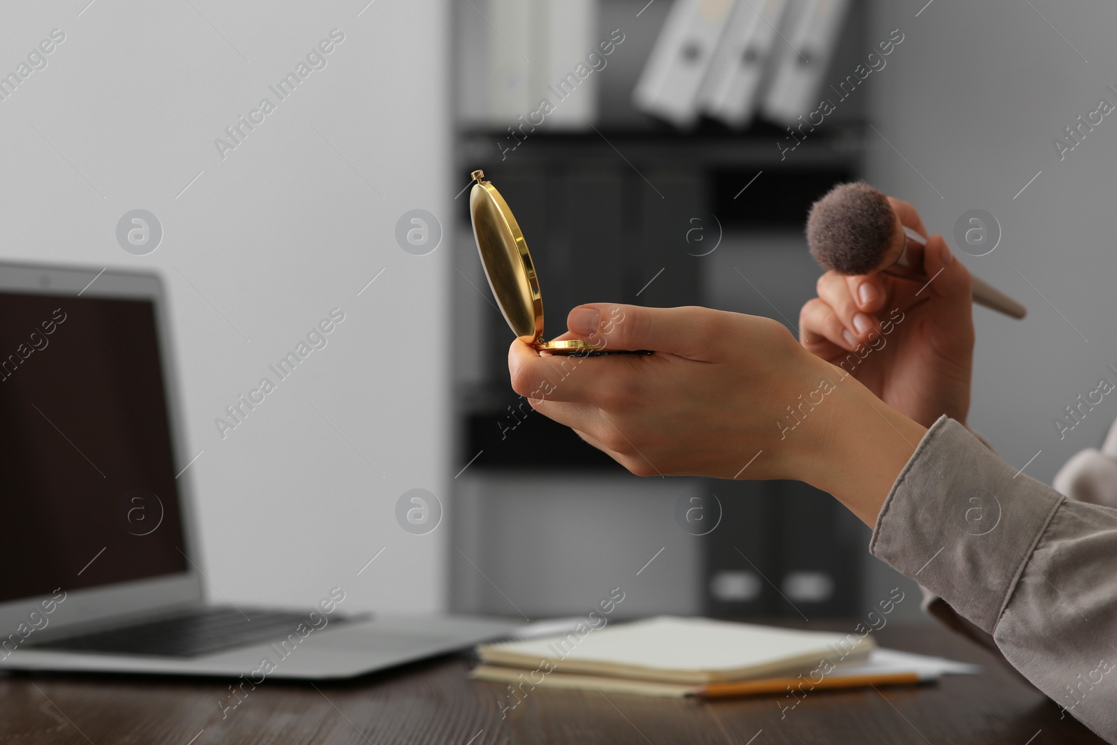 Photo of Woman with cosmetic pocket mirror and makeup brush at wooden table indoors, closeup. Space for text