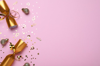 Photo of Open golden Christmas cracker and decorations with shiny confetti on pink background, flat lay. Space for text