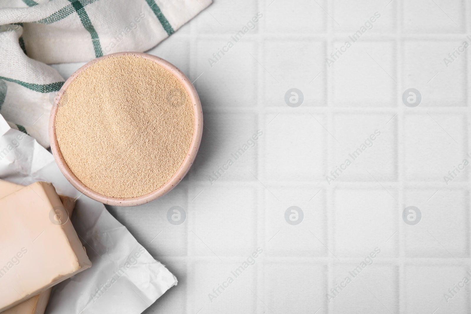 Photo of Granulated and compressed yeast in bowl on white tiled table, flat lay. Space for text