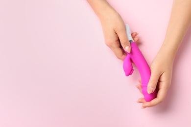 Photo of Young woman holding vibrator on pink background, top view with space for text. Sex toy