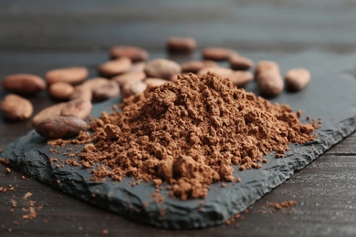 Slate plate with cocoa powder and beans on table