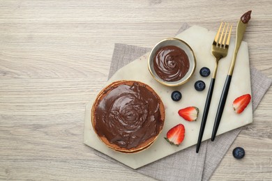 Photo of Delicious pancakes with chocolate paste, berries and cutlery on wooden table, top view. Space for text