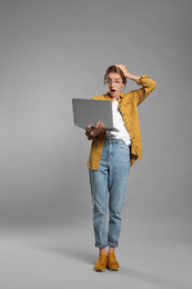 Full length portrait of emotional woman with modern laptop on grey background