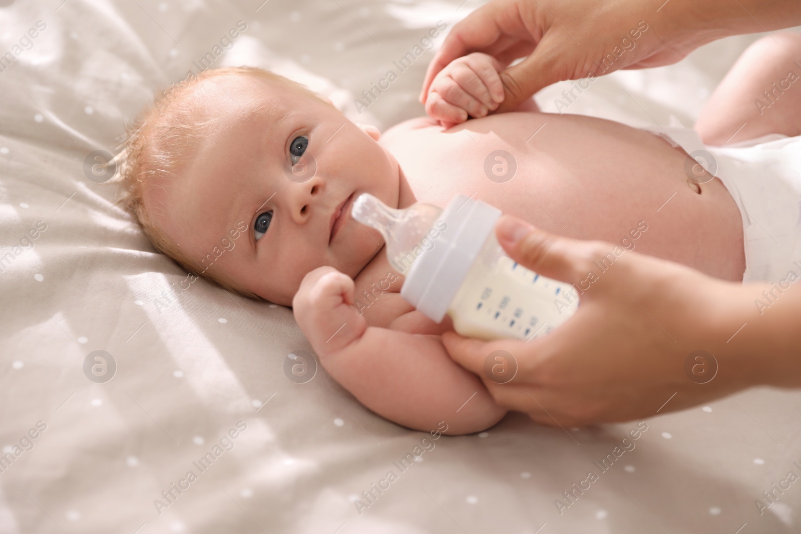 Photo of Mother feeding cute little baby with milk in cot, closeup. Healthy lifestyle