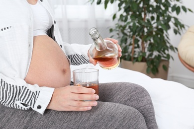 Photo of Pregnant woman pouring whiskey into glass at home. Alcohol addiction