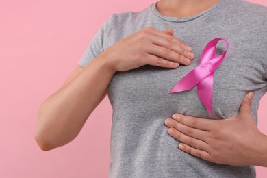 Woman with pink ribbon on color background, closeup. Breast cancer awareness
