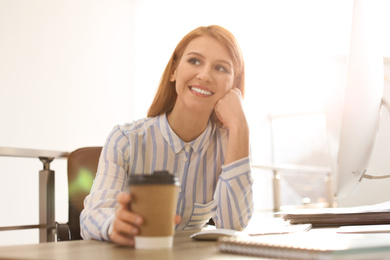 Young businesswoman with cup of coffee relaxing at table in office during break