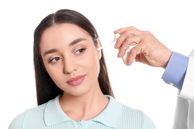 Doctor spraying medication into woman's ear on white background