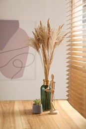 Photo of Dry plants on wooden table near window indoors. Interior design