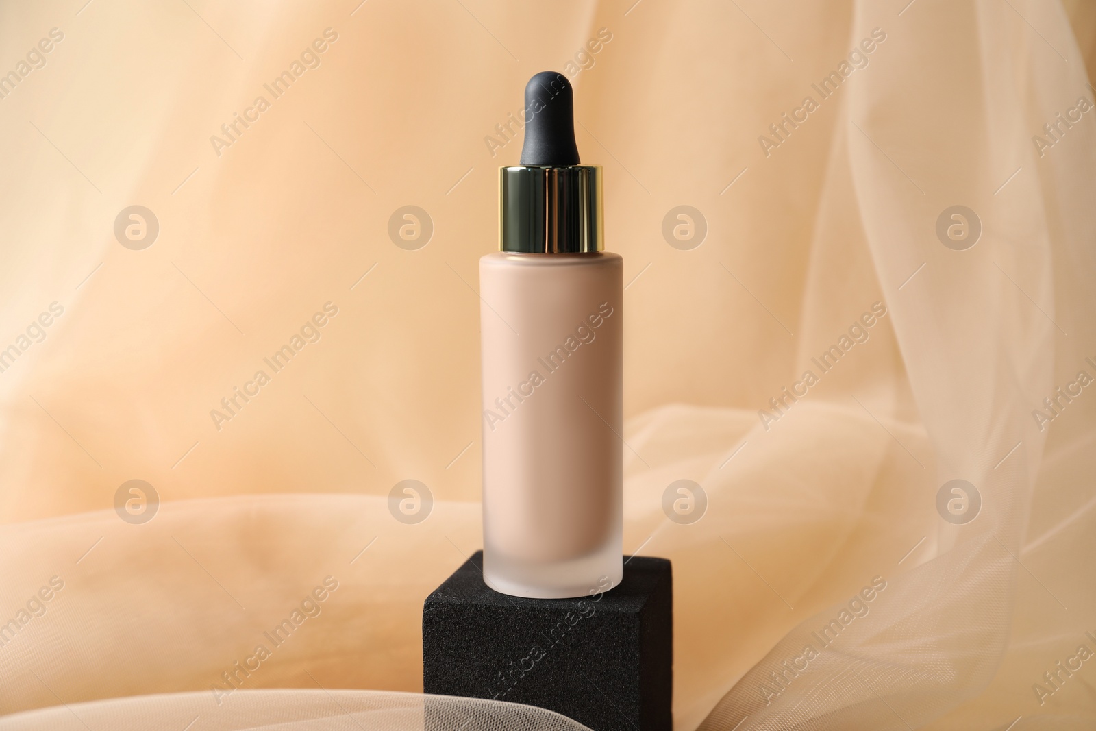 Photo of Bottle of skin foundation on beige tulle fabric. Makeup product