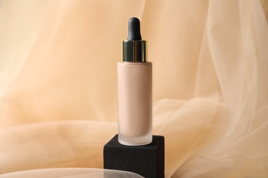 Bottle of skin foundation on beige tulle fabric. Makeup product