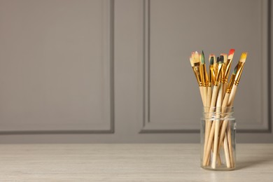Photo of Set of different paintbrushes in glass jar on white wooden table. Space for text