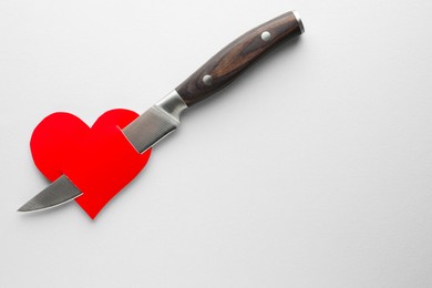 Broken heart. Red paper heart pierced with knife on white background, top view. Space for text