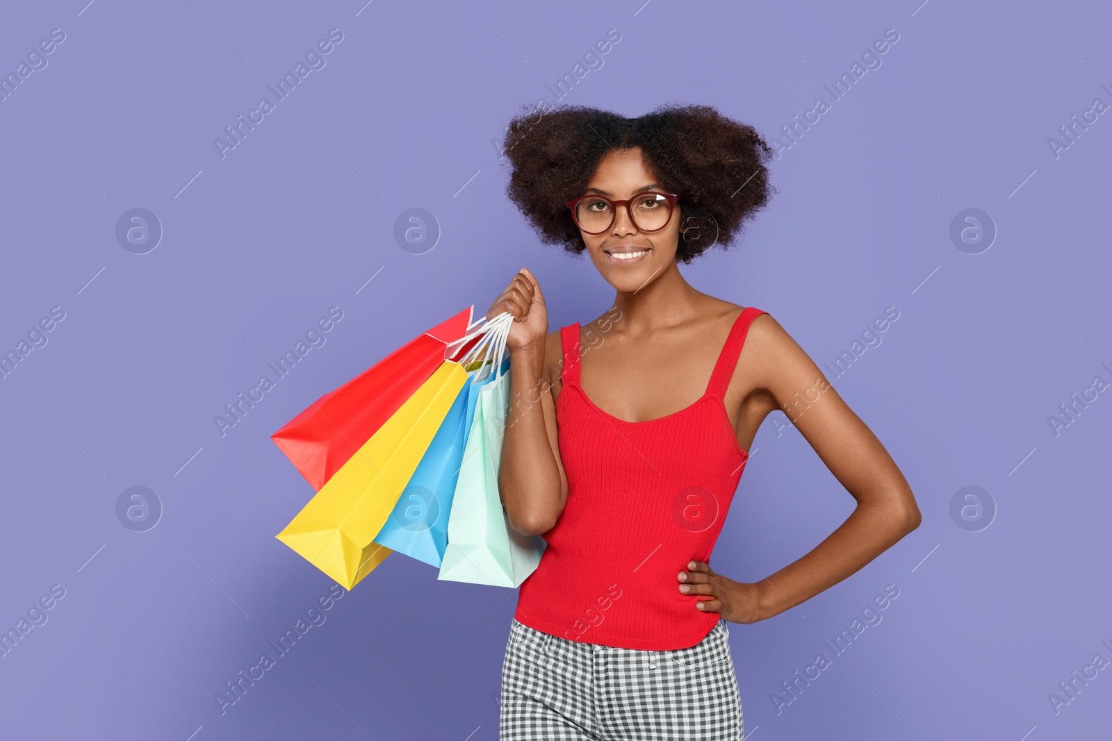 Photo of Happy African American woman in glasses with shopping bags on purple background