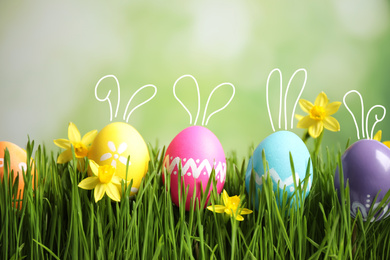 Image of Bright Easter eggs with cute bunny ears and flowers in green grass