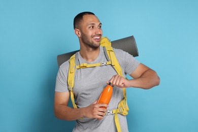 Photo of Happy tourist with backpack and thermo bottle on light blue background