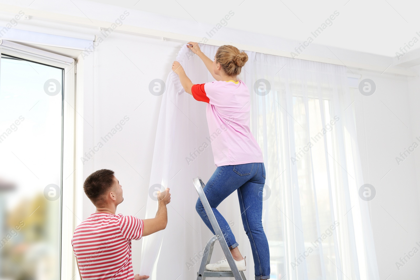 Photo of Young couple hanging window curtain indoors. Interior decor element