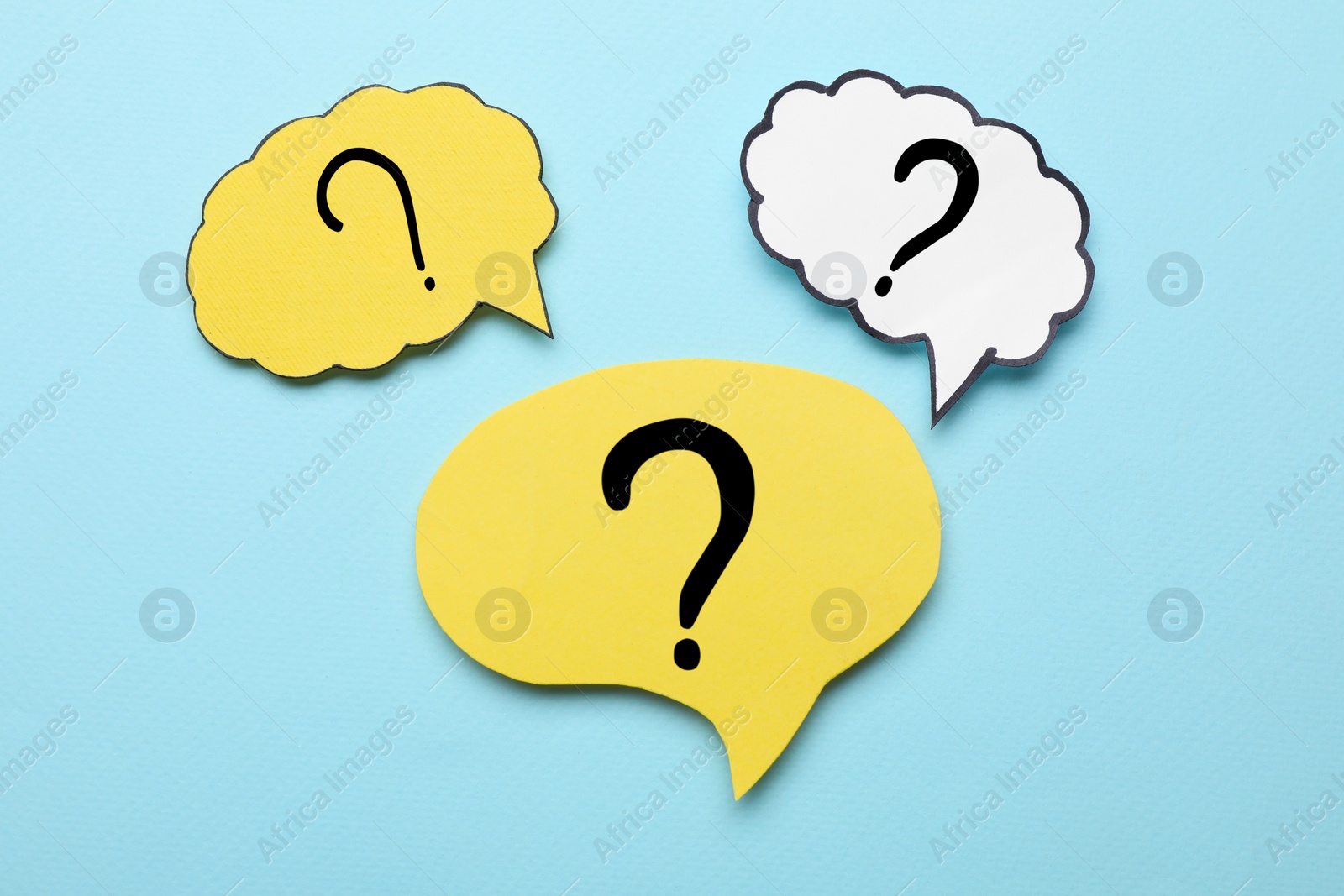 Photo of Paper speech bubbles with question marks on light blue background, flat lay