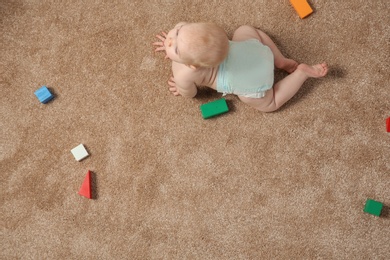 Cute little baby crawling on carpet with toys, top view. Space for text