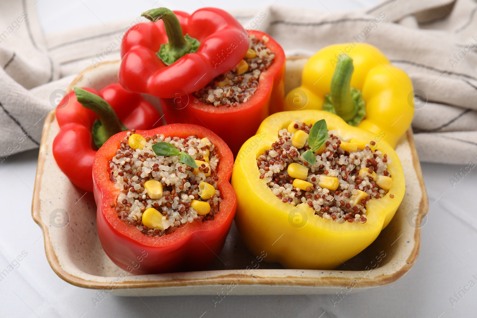 Photo of Quinoa stuffed bell peppers and basil in baking dish on white tiled table, closeup