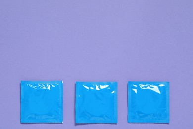 Photo of Condom packages on purple background, flat lay and space for text. Safe sex