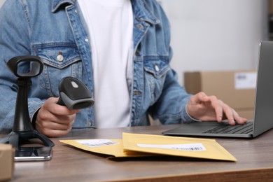Photo of Seller with scanner, parcels and laptop at table in office, closeup. Online store