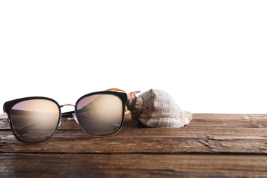 Photo of Stylish sunglasses and shells on wooden table against white background