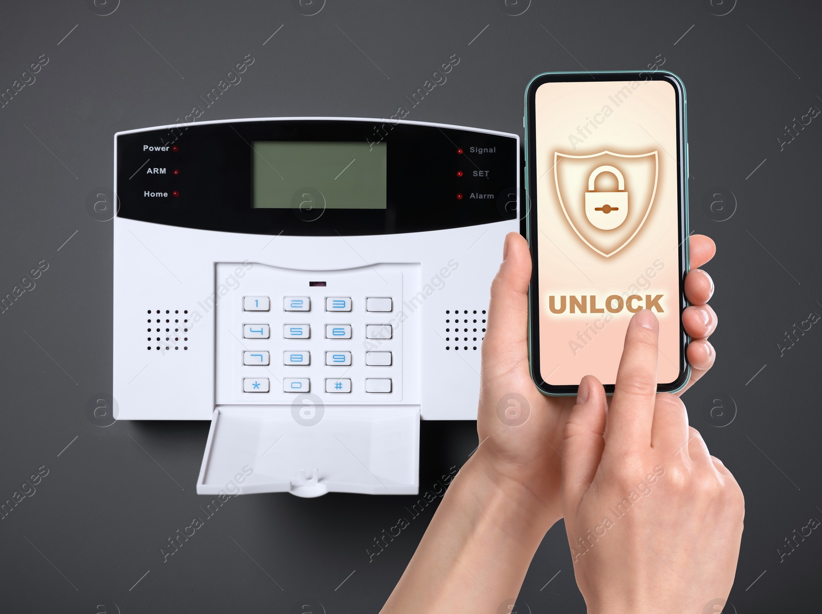 Image of Woman operating home alarm system via mobile phone against dark wall with security control panel, closeup. Application interface on device screen