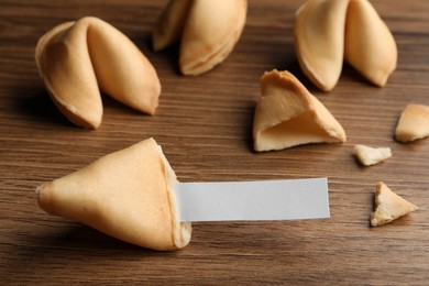 Tasty fortune cookies and paper with prediction on wooden table, closeup. Space for text