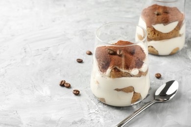 Delicious tiramisu in glasses, coffee beans and spoon on grey textured table, space for text